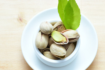  Pistachios on the white wooden background, accompanied by green leaf