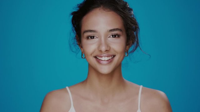 beautiful african girl with perfect natural skin and big lips smiling to the camera isolated on blue, young and clean female with naked shoulderds posing