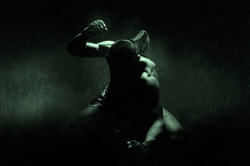 Kickboxer in the rain and under the green light of a spotlight. Mongkhon. The concept of losing in...