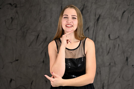 Universal concept of horizontal female portrait on gray alternative background. A photo of a pretty smiling girl with long hair and excellent make-up in a black dress stands in different poses.
