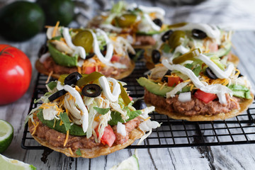 Chicken tostadas with refried pinto beans, fresh cilantro, shredded cheddar cheese, avocados, black olives, sour cream, lettuce, jalapenos, lime and tomatoes. Selective focus with blurred background.