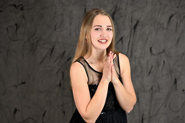 Fototapeta premium Universal concept of horizontal female portrait on gray alternative background. A photo of a pretty smiling girl with long hair and excellent make-up in a black dress stands in different poses.