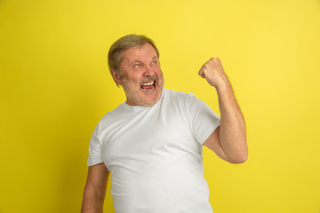 Celebrating winning. Caucasian man portrait isolated on yellow studio background. Beautiful male model in white shirt posing. Concept of human emotions, facial expression, sales, ad. Copyspace.