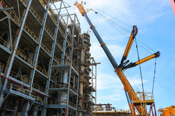 Fototapeta na wymiar Construction and installation work with a powerful construction crane of a large new industrial oil refining petrochemical chemical plant with pipes, columns, railings, stairs and equipment