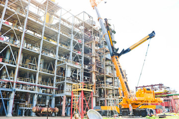Construction and installation work with a powerful construction crane of a large new industrial oil refining petrochemical chemical plant with pipes, columns, railings, stairs and equipment