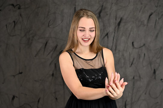 Universal concept of horizontal female portrait on gray alternative background. A photo of a pretty smiling girl with long hair and excellent make-up in a black dress stands in different poses.