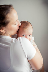 Young beautiful mother holds a baby. Mom kisses her baby. Children's bedroom.
