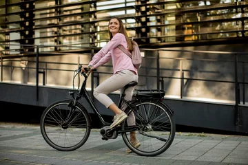 Poster Young woman riding e bike in urban enviroment © BGStock72