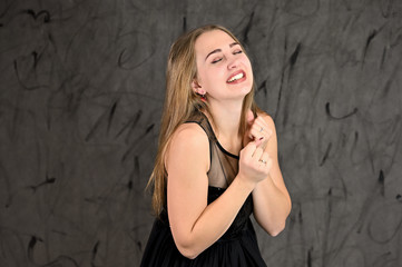 Fototapeta premium A photo of a pretty smiling girl with long hair and excellent make-up in a black dress stands in different poses. Universal concept of horizontal female portrait on gray alternative background.