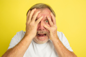 Shocked, scared, covering face with hands. Caucasian man portrait isolated on yellow studio background. Beautiful male model in white shirt. Concept of human emotions, facial expression, sales, ad.