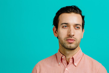 Fototapeta premium Portrait of a young adult man thinking, isolated on blue studio background
