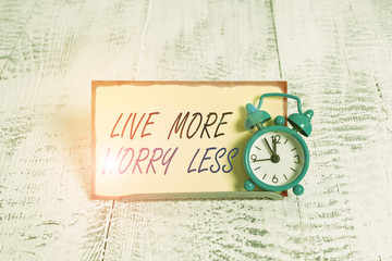 Writing note showing Live More Worry Less. Business concept for Have a good attitude motivation be careless enjoy life Alarm clock tilted above buffer wire in front of notepaper