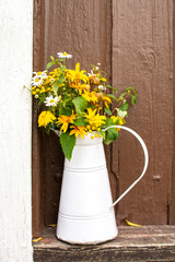 White jug with flowers in front of the wooden door, summer in countryside, Fagervik, Finland