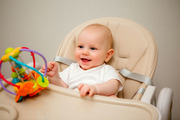 healthy baby boy with blue eyes sits in a high chair and plays with an educational toy