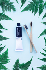 Two eco bamboo toothbrushes and charcoal mint natural toothpaste on blue background with fern leaves. Eco friendly concept. Zero waste. Top view.
