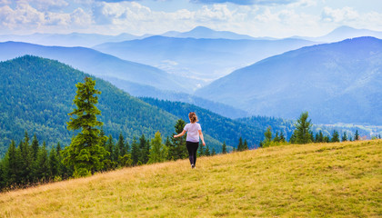Girl walking on the lawn on the background of majestic blue mountains_