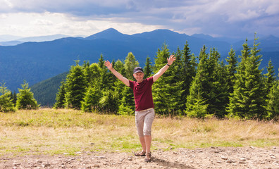 Man on the background of mountains with arms raised up shows joy and delight_