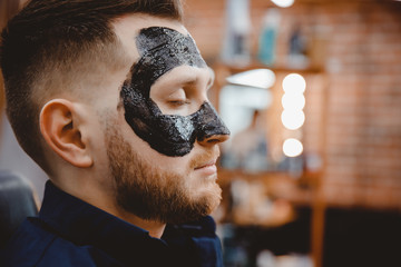 Handsome man with black charcoal face mask, concept skin care, pore cleansing from acne