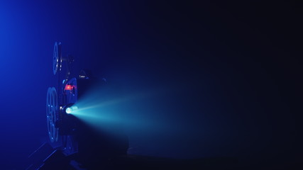 Working 8mm retro film projector in a dark blue smokey room. Front view, film projector projecting a beam of light