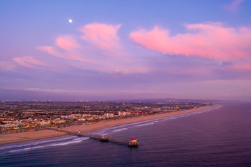 Aerial view of wooden pier in Huntington Beach, Orange County in California at sunset with waves crashing below at sunset, indicative of travel tourism and vacation time.