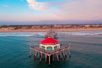 Aerial view above the Huntington Beach Pier in Orange County, California on a sunny day with ocean water below and people walking on pier.