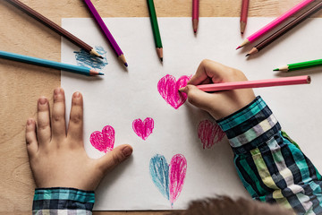 Baby hand with pencil heart drawing. Concept for Valentines Day or Mother's Day or Father's Day. A child draws a heart with pencil/pen. Top View.