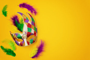 Festive, colorful mardi gras or carnivale mask and accessories over yellow background. Party invitation, greeting card, venetian carnivale celebration concept. Flat lay, top view, copy space - obrazy, fototapety, plakaty