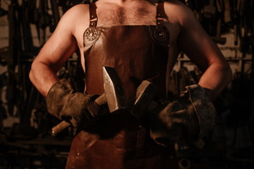 Fototapeta na wymiar Brutal artisan blacksmith standing in a workshop with two hammers close up