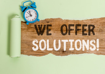Conceptual hand writing showing We Offer Solutions. Concept meaning Offering help assistance Experts advice strategies ideas Alarm clock and torn cardboard on a wooden classic table backdrop