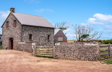 Fototapeta na wymiar Stanley, Tasmania, Australia - December 15, 2009: Hightfield Historic Site. Small gray stone house with adjacent wall and fences under blue sky with some white clouds.