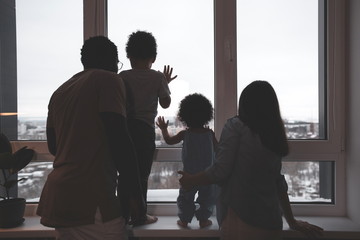 Happy family with two children looking out the window standing in the apartment