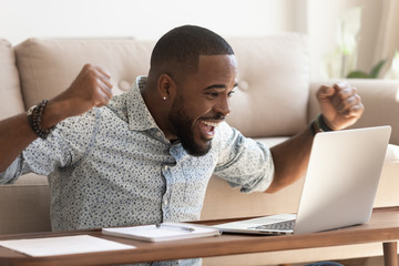 Excited african man read message on computer celebrating received opportunity