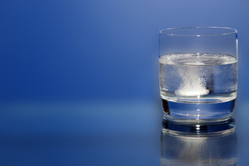 pill for headache or cold in a glass of water on a blue background, health care