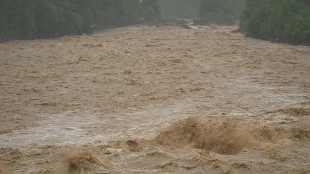 Fast flowing raging river. Soil and mud is moving towards down. After strong rain. Giant roiling brown muddy water. Foamy stream dangerous wild brook. Swollen boiling creating. Damage environmentally.