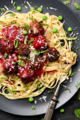 Nordic style meal. Linguine pasta and homemade meatballs with green peas, lingonberry sauce and cheese on grey plate on black background