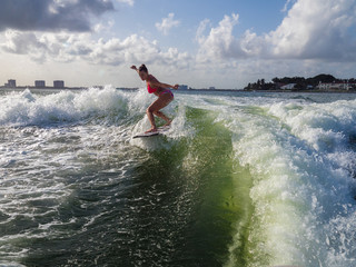 Pretty woman balances over wave, wakesurfing at sea, water splashing
