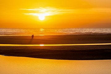 Beautiful ocean sunset with silhouette of couple walking along the beach. © Lux Blue
