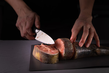 cook cuts the fish into pieces with a knife on a gray board on a concrete background