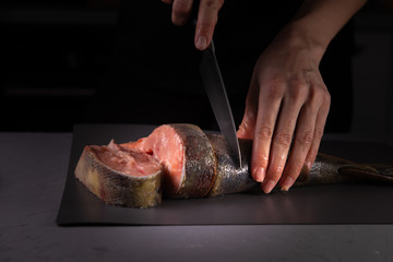 cook cuts the fish into pieces with a knife on a gray board on a concrete background