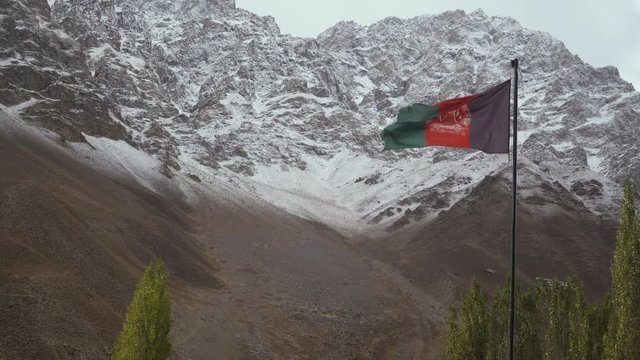 afghanistan flag waving in the wind against the backdrop of snowy mountains