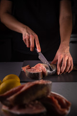 cook cuts the fish into pieces with a knife on a gray board on a concrete background