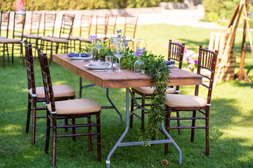 Beautifully decorated wooden table in a summer open-air cafe. Green branch and fresh flowers table decoration
