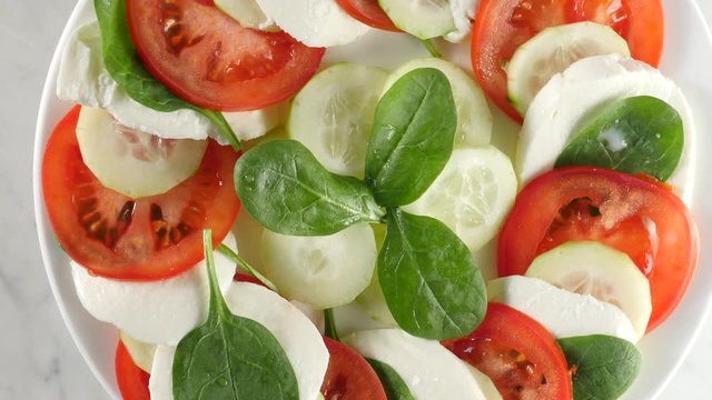 caprese salad top view. Healthy vegetarian salad with sliced tomatoes, cucumber, mozzarella and basil. Fresh, natural summer dinner. White plate and background