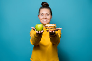 girl holds an apple and a burger on the palms, handing them to the viewer to choose