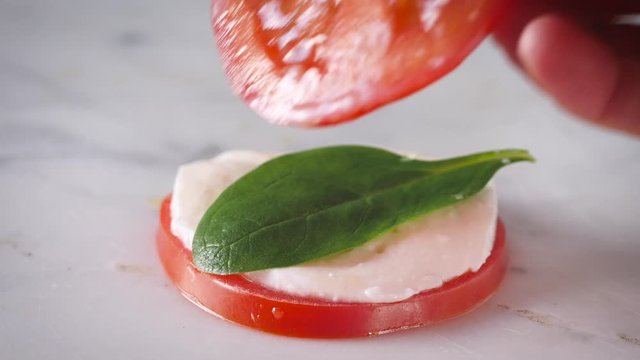 Preparing sandwich, tower caprese salad. Healthy vegetarian salad with sliced tomatoes, cucumber, mozzarella and basil. Fresh, natural summer dinner. White plate