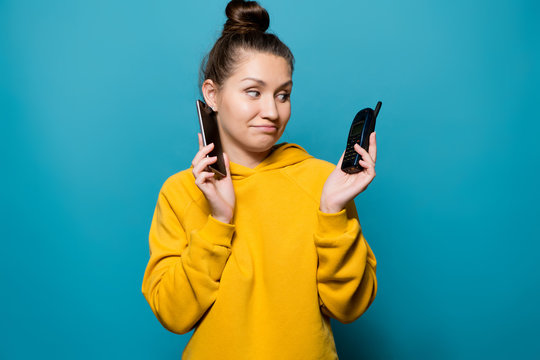 girl puts a smartphone to her ear and looks at the old cell telephone with a sad smile