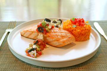 Grilled salmon steak with Mediterranean salsa and saffron rice on white plate