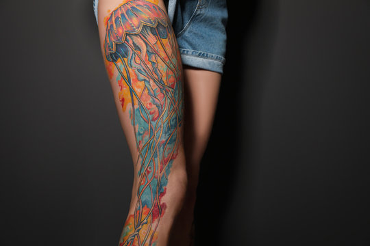 Woman with tattoos on leg against black background, closeup