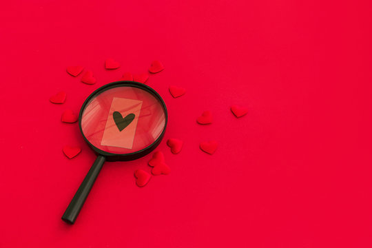Black heart through a magnifying glass among red hearts on red background. Valentine day concept, searching for special love concept.