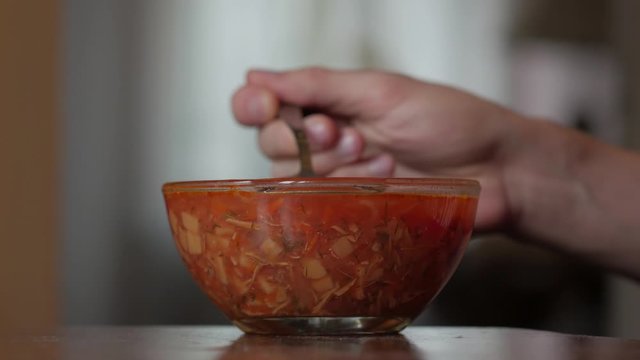 Man eating red soup male hand eats borscht with a spoon from a transparent plate closeup